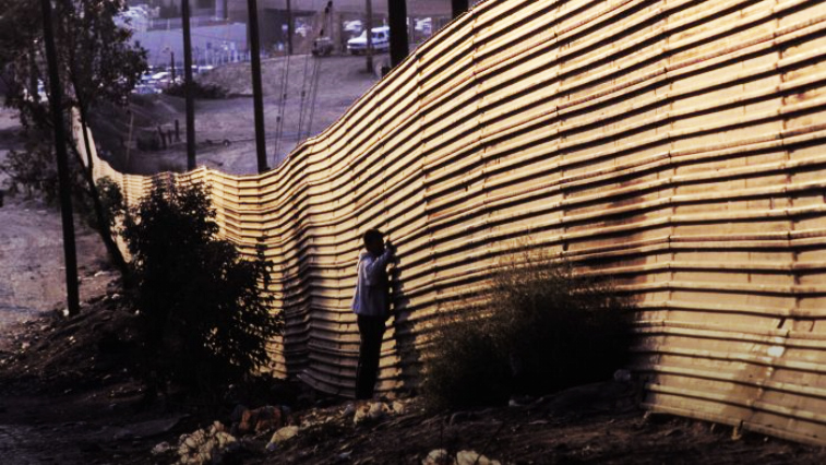 Image of person standing at a metal border wall